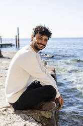 Portrait of smiling young man sitting at Lake Garda, Italy - GIOF08119