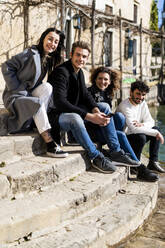 Porträt von vier Freunden, die auf einer Treppe am Gardasee sitzen, Italien - GIOF08124