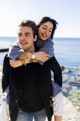 Porträt eines jungen Mannes, der seine Freundin huckepack trägt, am Gardasee, Italien - GIOF08128