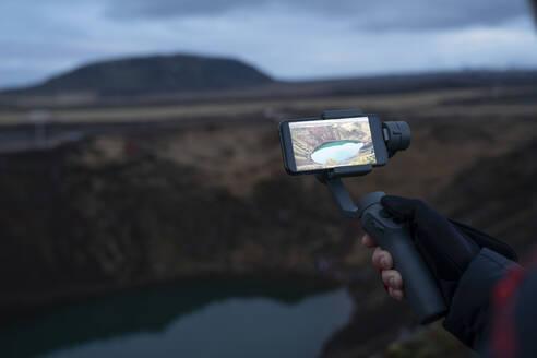 Island, Hand einer Person, die einen Kratersee fotografiert - DAMF00359