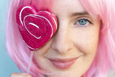 Portrait of young woman wearing pink wigwith heart-shaped lolly covering her eye - AFVF06093