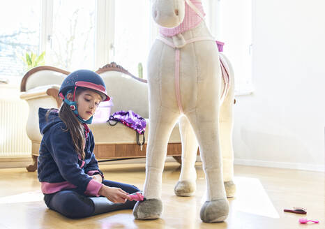 Mädchen striegelt ihr Spielzeugpferd zu Hause - DIKF00466