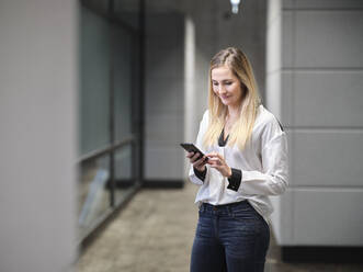 Smiling businesswoman using cell phone in modern office - CVF01577