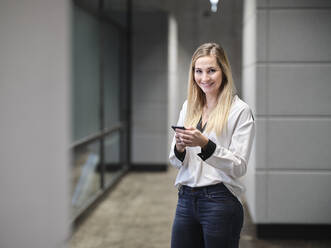 Smiling businesswoman using cell phone in modern office - CVF01578