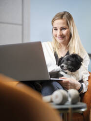 Geschäftsfrau mit Hund im Sessel sitzend mit Laptop - CVF01585
