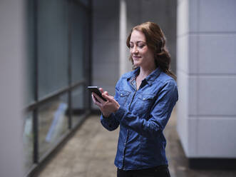 Lächelnde Geschäftsfrau, die ein Mobiltelefon in einem modernen Büro benutzt - CVF01588