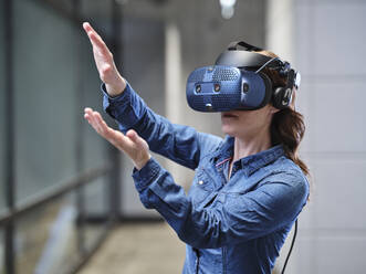 Woman wearing VR glasses and headset in modern office - CVF01594