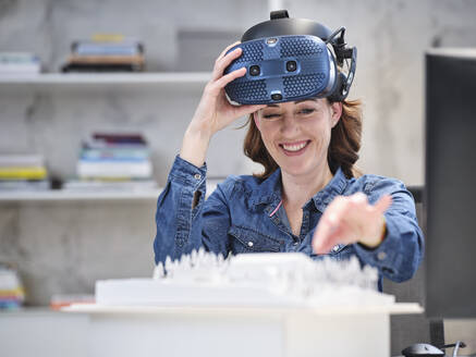 Smiling woman taking off VR glasses in modern office - CVF01596