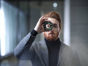 Portrait of businessman looking through an object in modern office - CVF01617