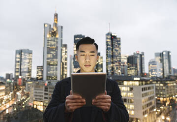 Mann mit Tablet vor der städtischen Skyline in der Abenddämmerung, Frankfurt, Deutschland - AHSF02255