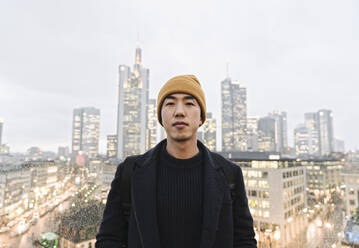 Portrait of stylish man in front of urban skyline, Frankfurt, Germany - AHSF02257