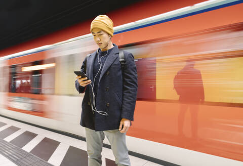 Stylish man with smartphone and earphones in metro station - AHSF02263