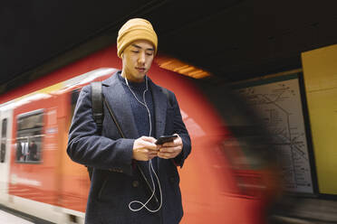 Stilvoller Mann mit Smartphone und Kopfhörern in der U-Bahn-Station - AHSF02264