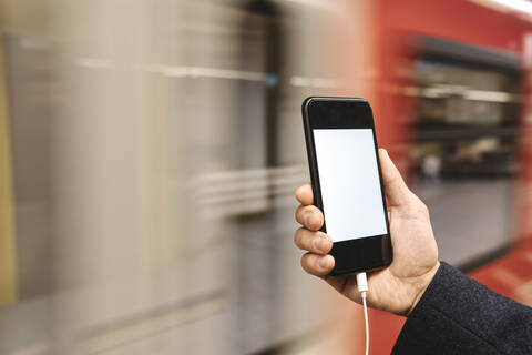 Close-up of man holding smartphone in metro station stock photo