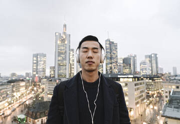 Mann mit Kopfhörern vor städtischer Skyline, Frankfurt, Deutschland - AHSF02285