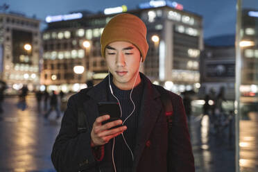 Man with earphones using smartphone in the city at night - AHSF02288