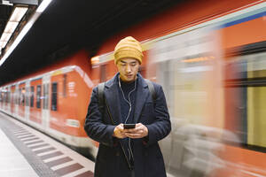 Stilvoller Mann mit Smartphone und Kopfhörern in der U-Bahn-Station - AHSF02291