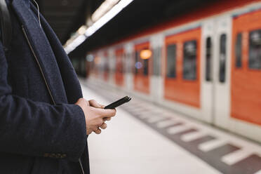 Nahaufnahme eines Mannes, der in einer U-Bahn-Station sein Smartphone benutzt - AHSF02292