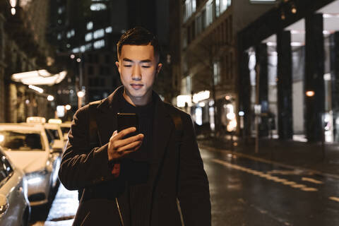 Man using smartphone while walking in the city at night stock photo