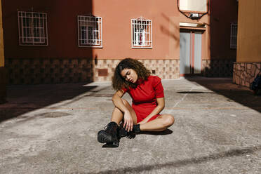 Young woman wearing red dress and sitting on ground - TCEF00499