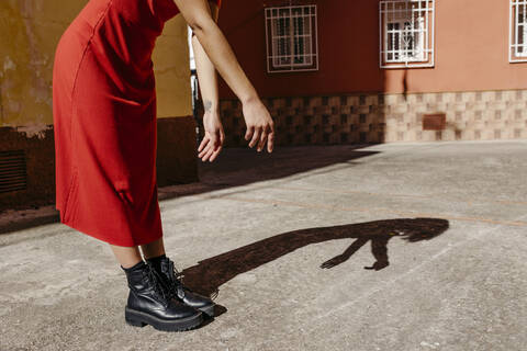 Junge Frau in rotem Kleid und schwarzen Stiefeln, die mit ihrem Schatten auf dem Boden spielt, lizenzfreies Stockfoto