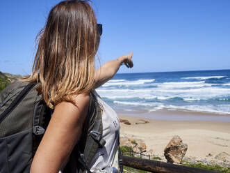 Backpack woman pointing with her finger out to the ocean, Robberg Nature Reserve, South Africa - VEGF01890