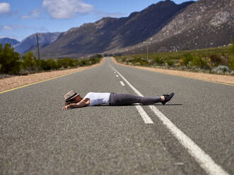 Woman lying in the middle of a road surrounded by mountains, Swellendam area, South Africa - VEGF01892