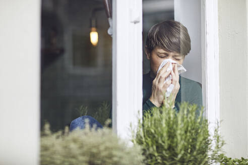 Woman blowing her nose at home at the window - MCF00662