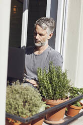 Älterer Mann sitzt zu Hause am Fenster und benutzt einen Laptop - MCF00672