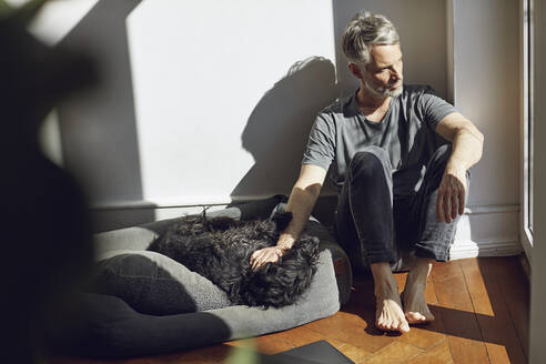Älterer Mann sitzt zu Hause mit Hund auf dem Boden - MCF00680