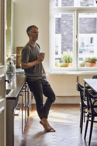 Älterer Mann hält Tasse in der Küche zu Hause, lizenzfreies Stockfoto