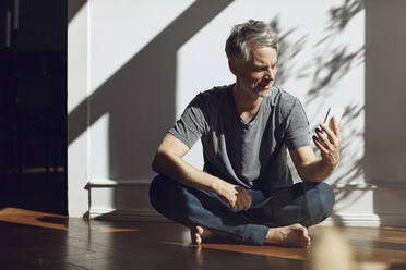 Mature man sitting on the floor at home using cell phone - MCF00692