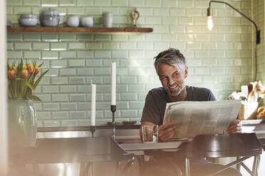 Lächelnder reifer Mann sitzt in der Küche und liest Zeitung - MCF00702
