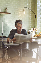 Älterer Mann sitzt in der Küche und liest Zeitung - MCF00703