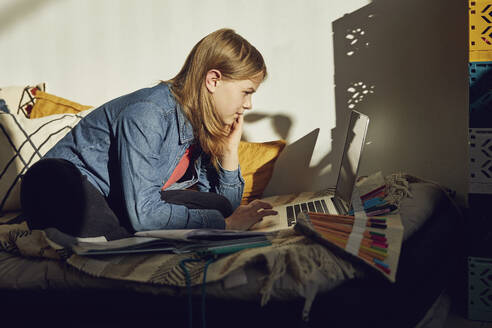 Girl sitting on bed at home doing homework and using laptop - MCF00706