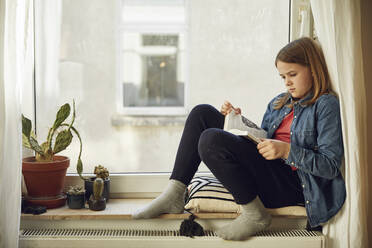 Mädchen sitzt zu Hause am Fenster und liest ein Buch - MCF00712