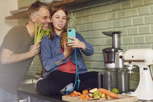 Glücklicher Vater und Tochter in der Küche machen ein Selfie mit Obst und Gemüse - MCF00718