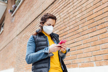 Woman covering her face with protective mask and using smartphone - JCMF00585