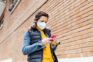 Woman covering her face with protective mask and using smartphone - JCMF00585