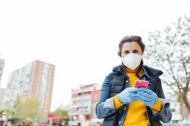 Woman wearing protective mask and using smartphone in the city - JCMF00587