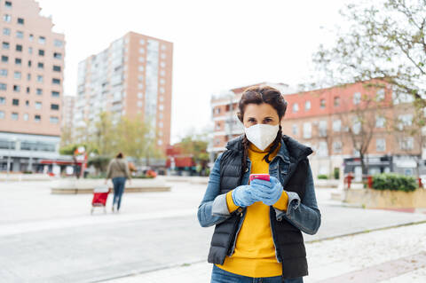 Woman wearing protective mask and using smartphone on square stock photo