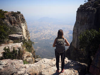 Rückenansicht einer Frau mit Rucksack, die auf einem Felsen steht und die Aussicht genießt, Tundavala, Angola - VEGF01944