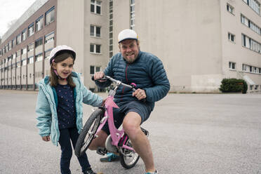 Playful father with daughter on her bicycle - JOSEF00289