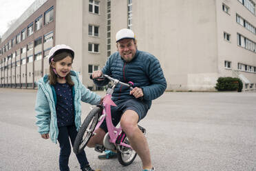 Verspielter Vater mit Tochter auf ihrem Fahrrad - JOSEF00289