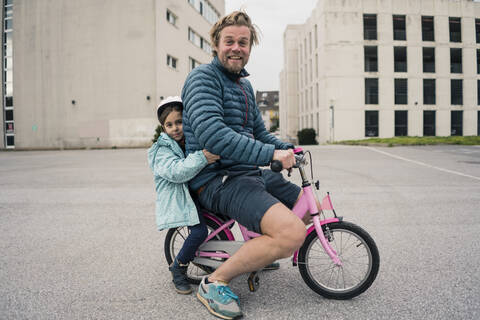 Verspielter Vater mit Tochter auf ihrem Fahrrad, lizenzfreies Stockfoto