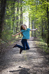 Portrait of girl jumping in the air on forest track - LVF08836