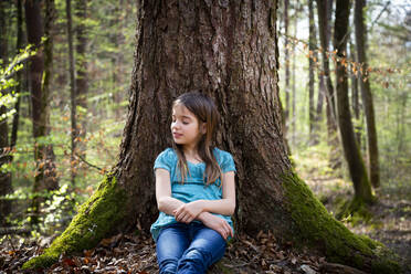 Portrait of girl with eyes closed leaning against tree trunk in forest - LVF08837