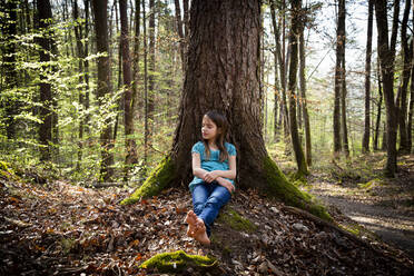 Girl with eyes closed leaning against tree trunk in forest - LVF08838