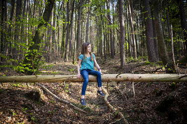 Smiling girl sitting on deadwood in forest - LVF08842