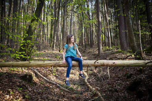 Lächelndes Mädchen sitzt auf Totholz im Wald - LVF08842